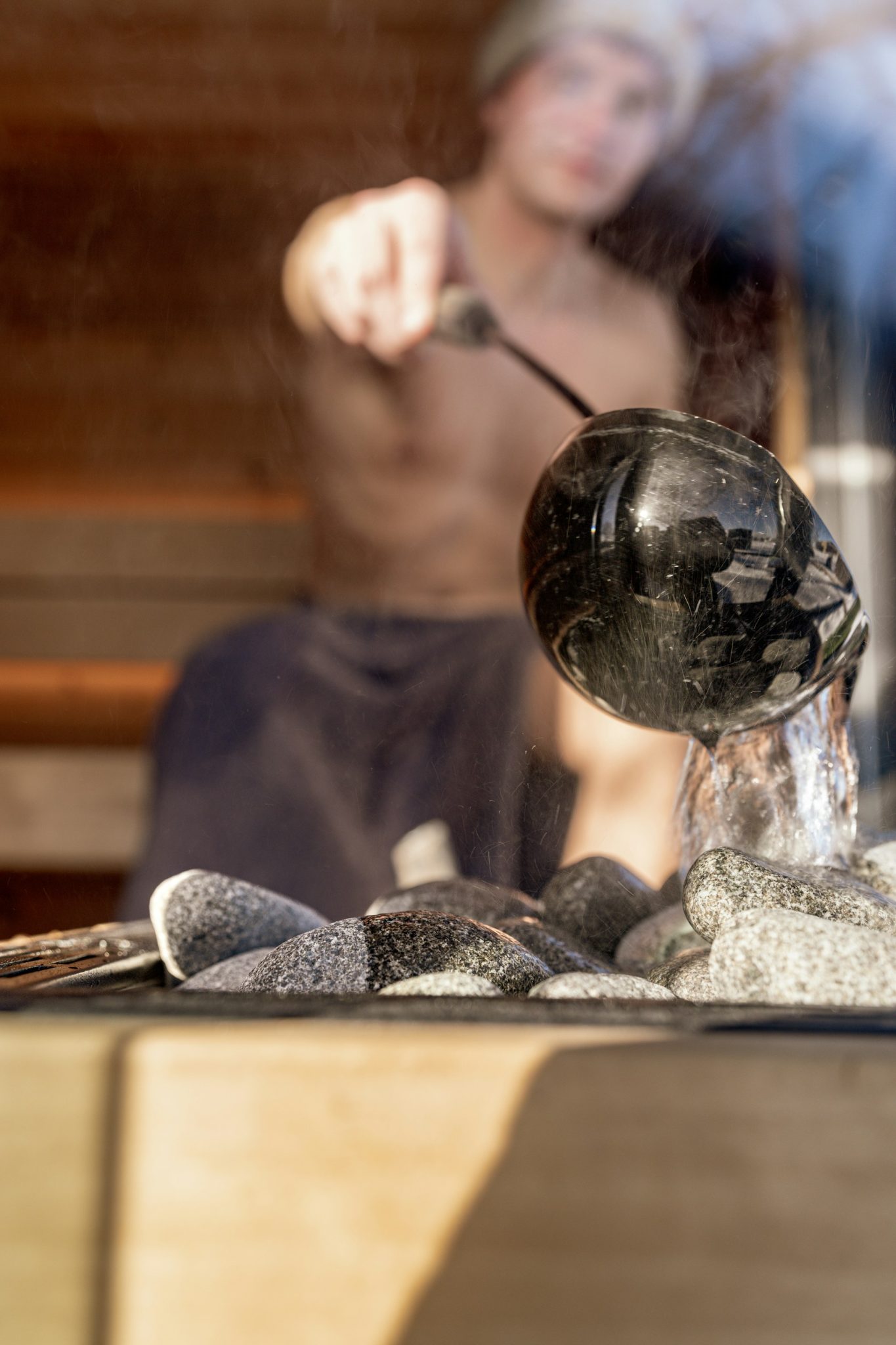 Image of a man pouring water on steaming sauna rocks