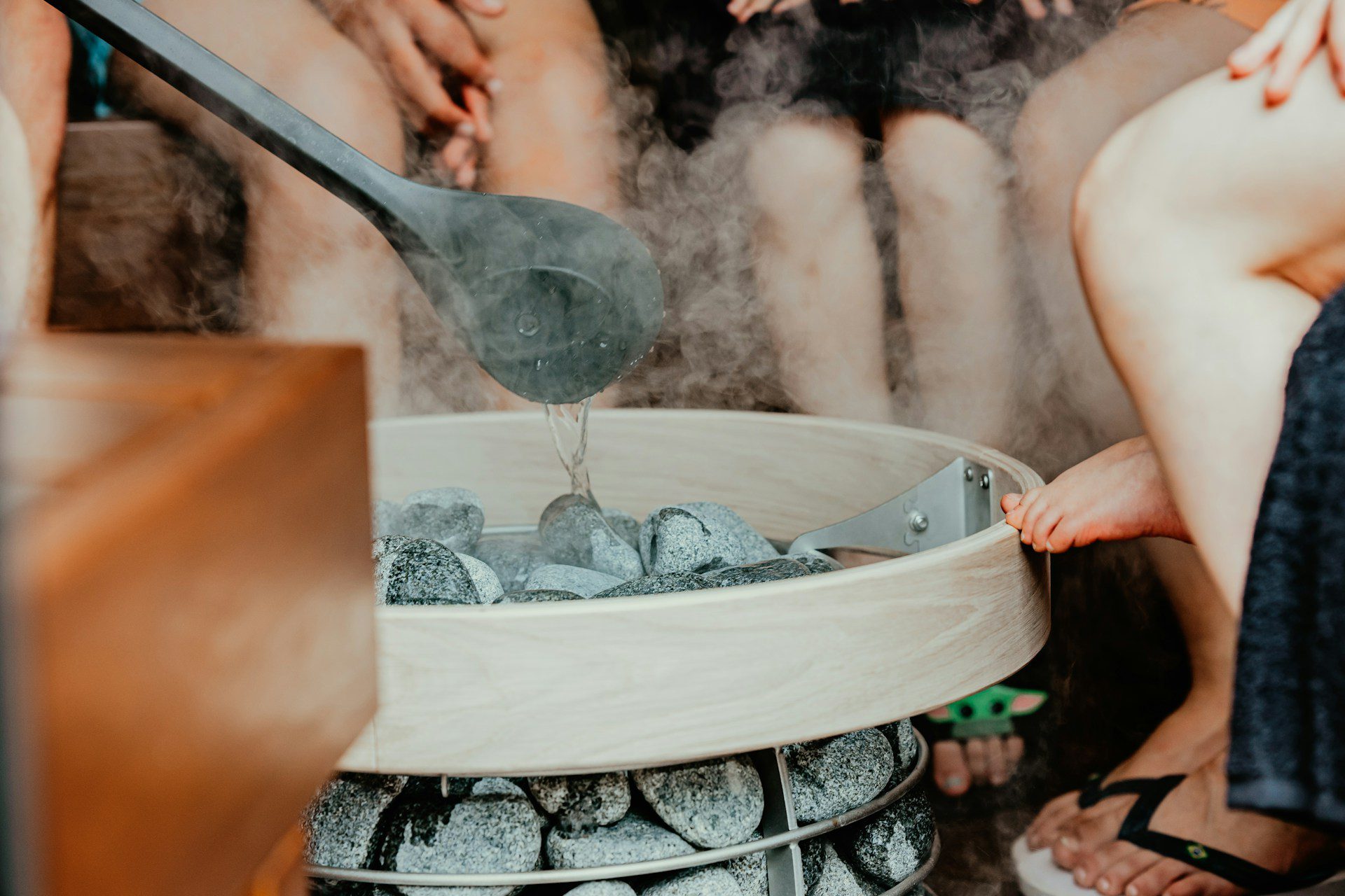 Someone putting water on rocks in a sauna to make it steamy. Other people are sitting around.