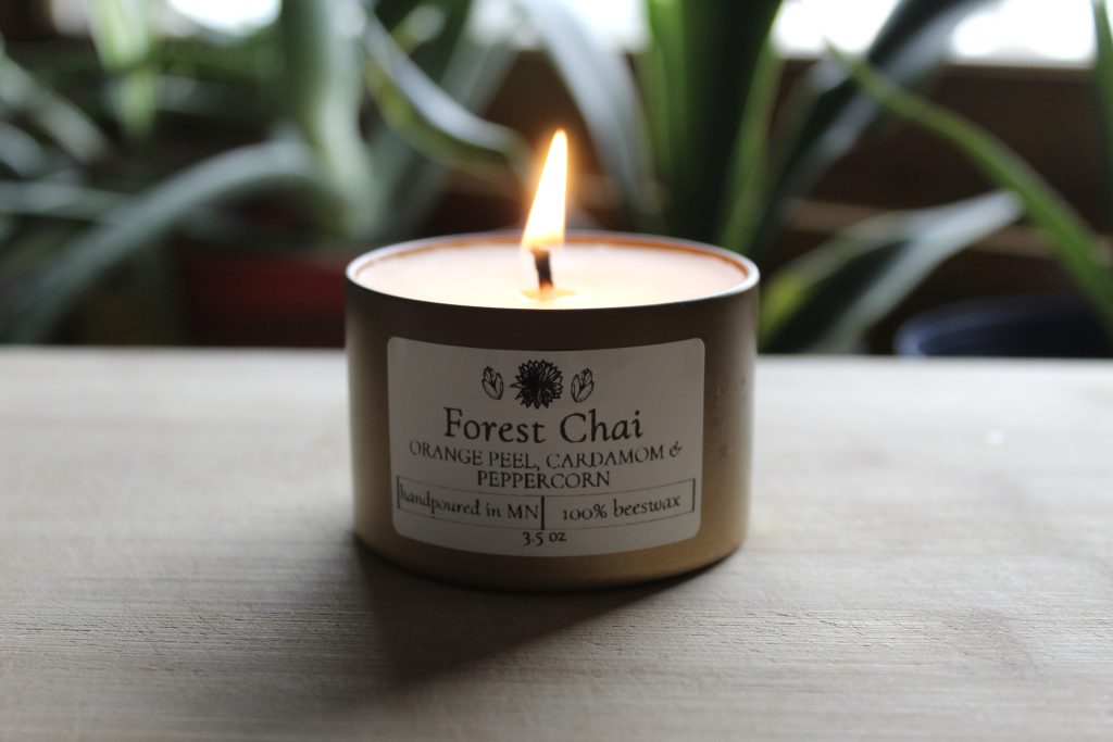Image of a lit candle that's scented Forest Chai among a blurry backdrop