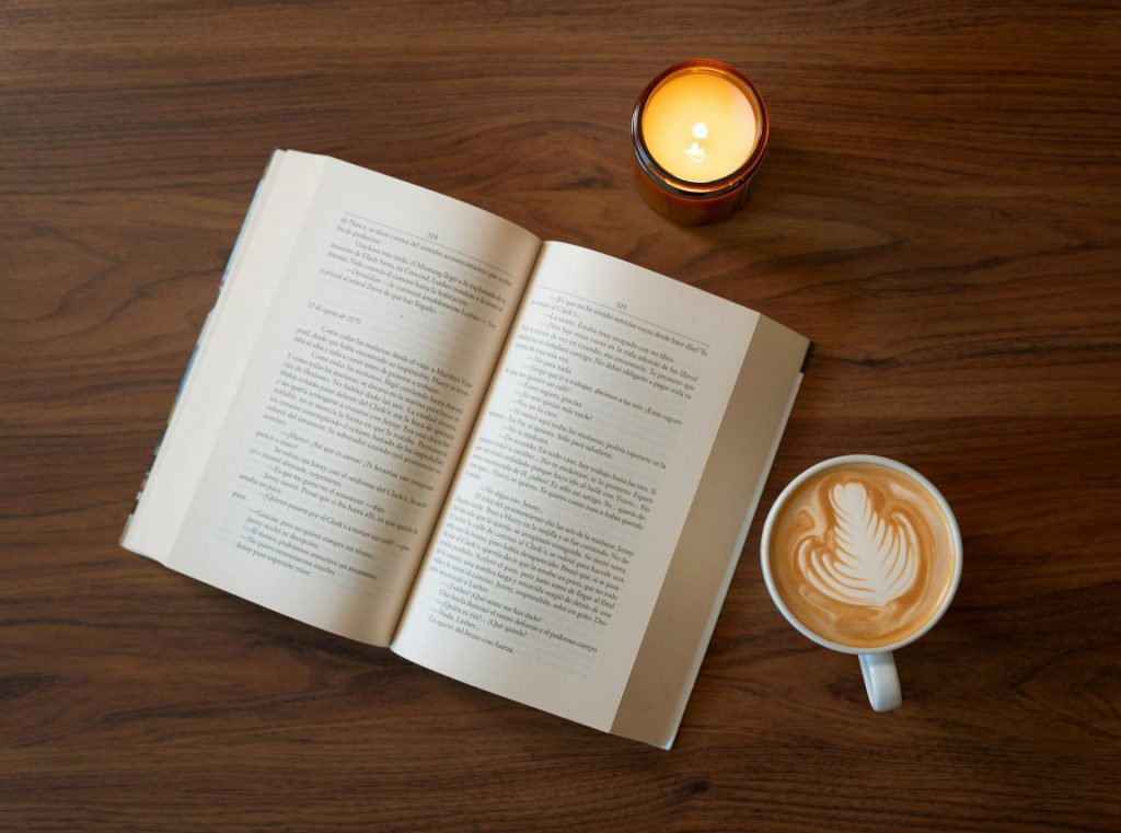 Image of an open book on a table, with a lit candle and hot latte sitting next to it