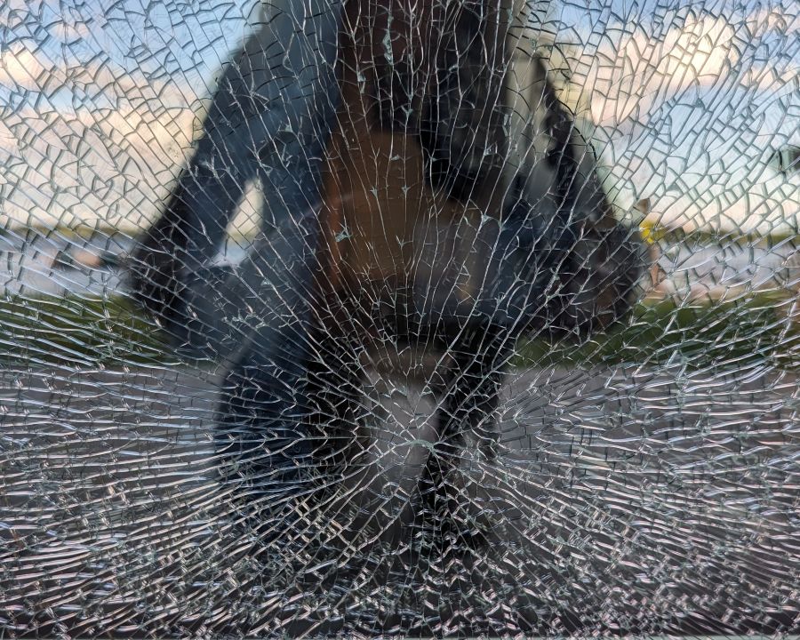 A person's reflection shows in the broken glass of a window