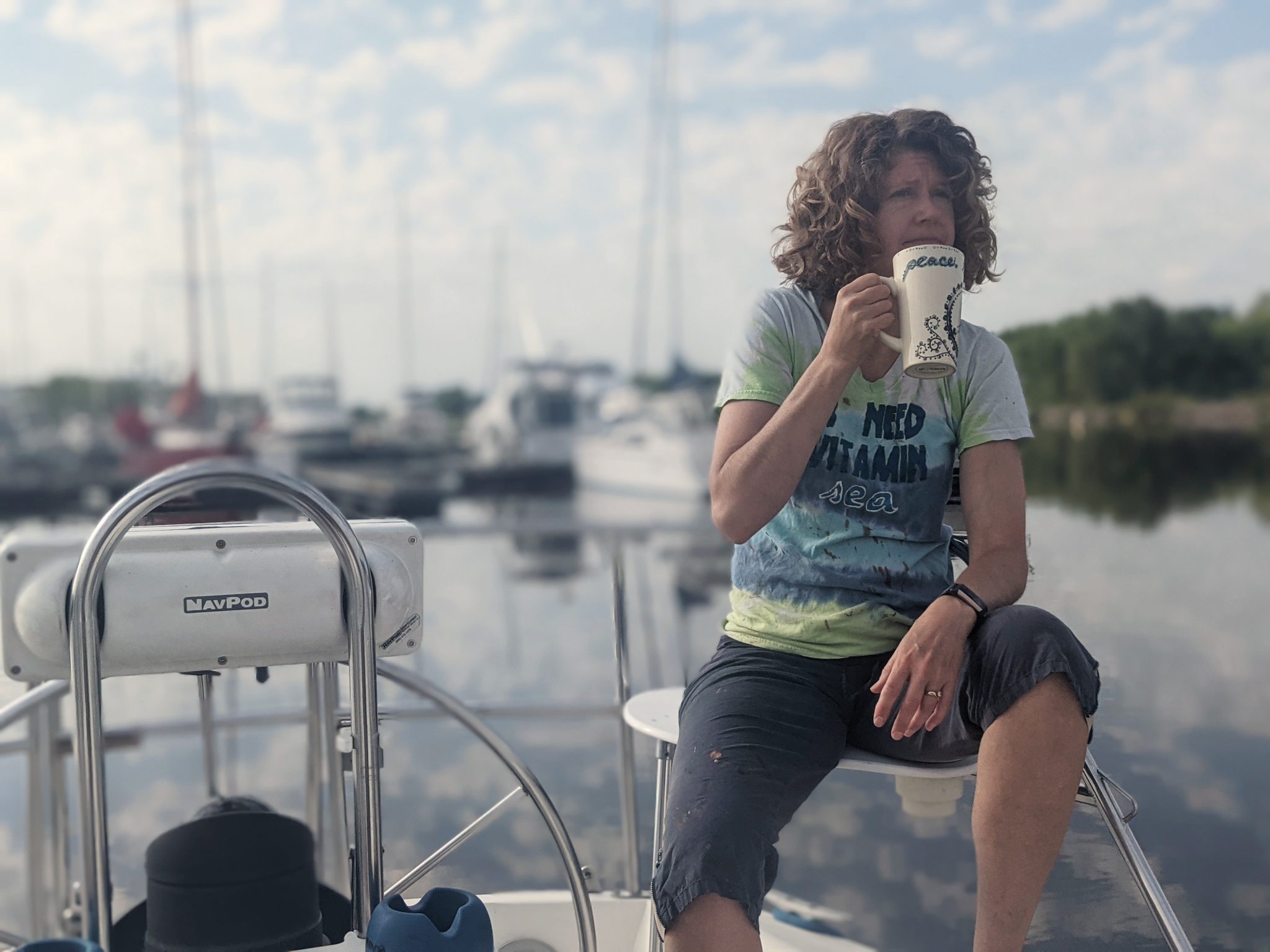 A woman drinks coffee on a sailboat in a marina