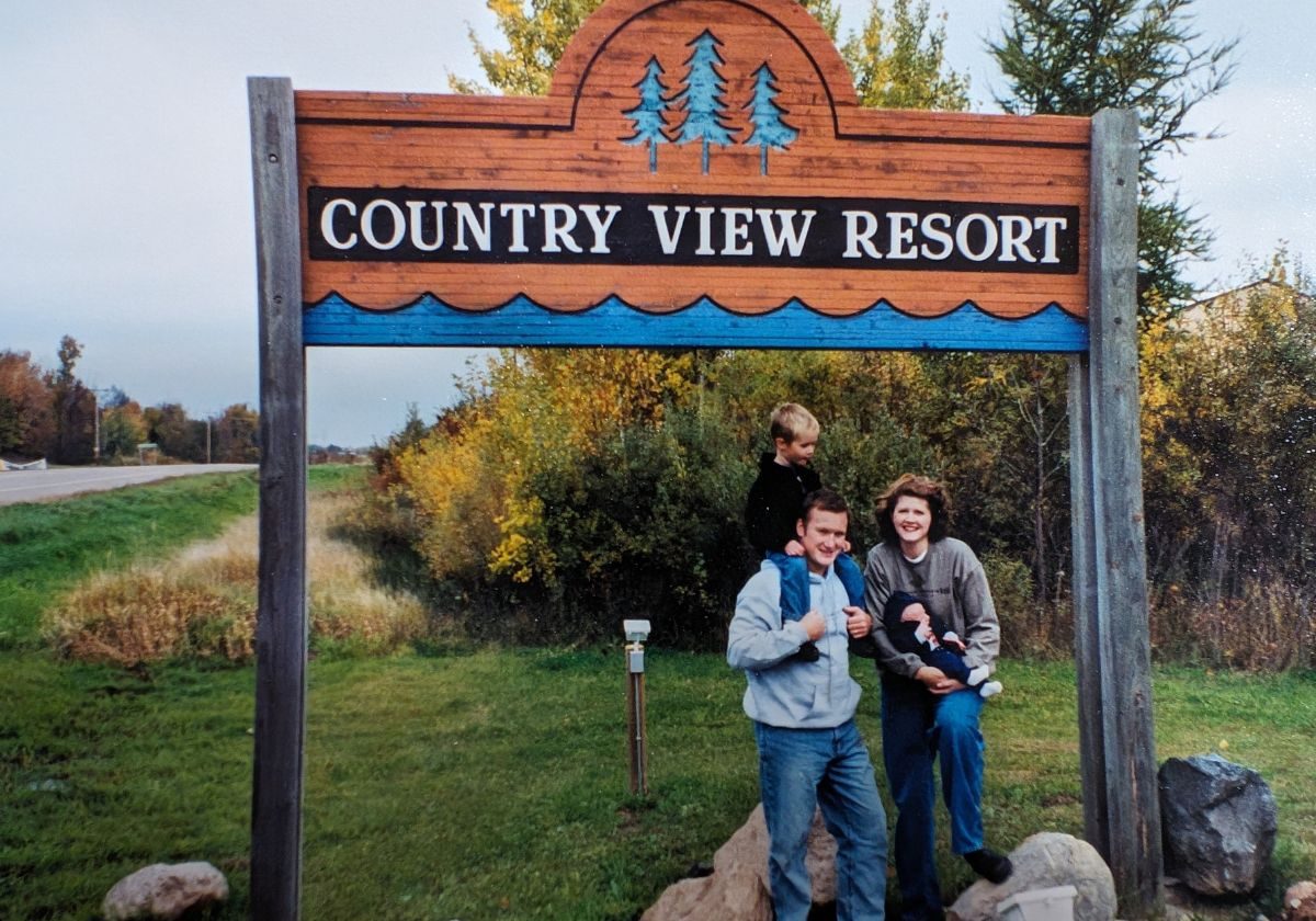 A young family stands in front of the sign of the resort they just bought, a goal achieved.